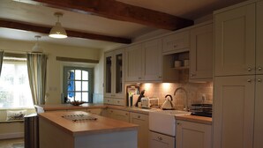 A kitchen with a central island, wooden beams on the ceiling, and light-colored cabinets.