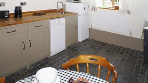 Une cuisine compacte équipée d’un évier, d’un four à micro-ondes et d’un lave-vaisselle. Une table recouverte d’une nappe à carreaux et une chaise se trouvent au premier plan.