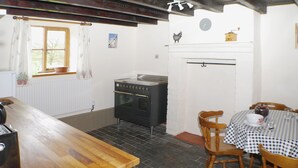Une cuisine équipée d’une cuisinière, de chaises, d’une table et d’une fenêtre avec des rideaux.