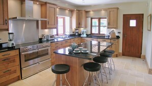 Une cuisine moderne avec des meubles en bois, un îlot central doté de tabourets, des appareils en acier inoxydable et une grande fenêtre.