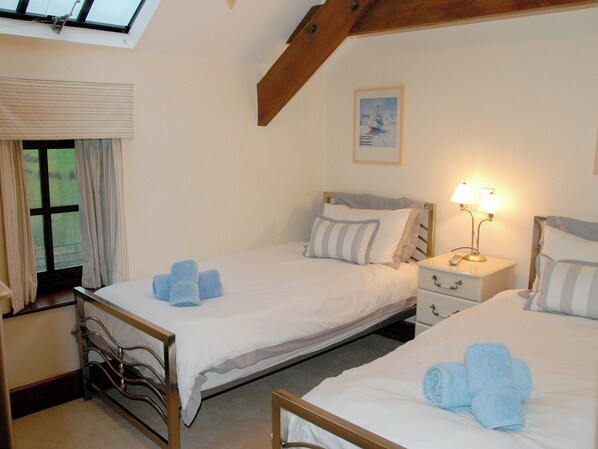 Une chambre avec deux lits, une fenêtre avec des rideaux, une table de chevet avec une lampe et un tableau au mur.