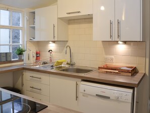 A modern kitchen with white cabinets, a Bosch dishwasher, a sink, and a window with a view of trees.