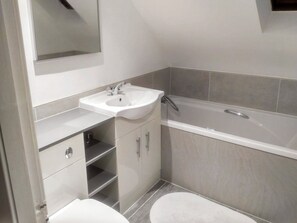 A compact bathroom with a white sink, a mirror above it, a toilet, and a bathtub.