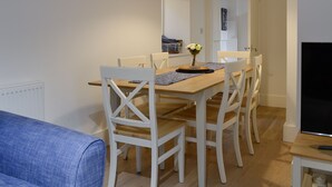 Een eetruimte met een houten tafel, witte stoelen, een bloemenvaas en een hanglamp.