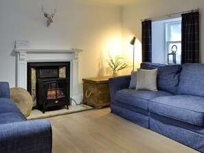 A living room with a fireplace, a sofa, a wooden chest, and a lamp. - 3 bedroom accommodation in Cullen (Cullen)