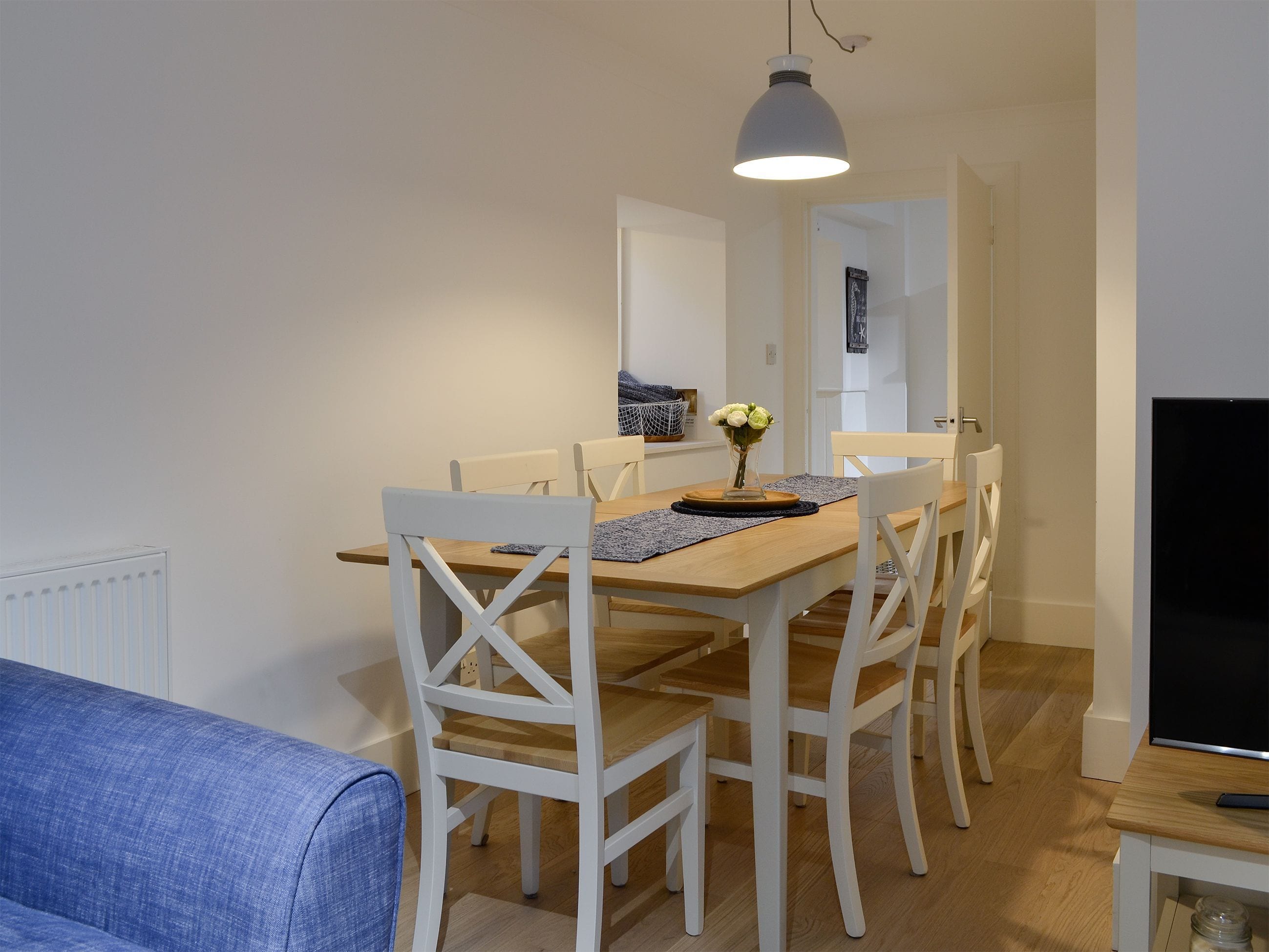 A dining area with a wooden table, white chairs, a vase with flowers, and a hanging light fixture.