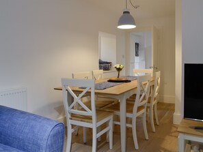 A dining area with a wooden table, white chairs, a vase with flowers, and a hanging light fixture.