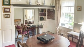 A dining area with a round table, chairs, a bookshelf, and a window with curtains.