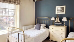 A bedroom with a bed, bedside table, lamp, and a window with a view of the street.