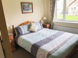 A neatly made bed with patterned bedding, a wooden headboard, and a framed picture above it. - 4 bedroom accommodation in Near Ely (Near Ely)