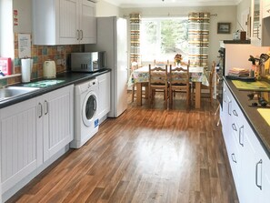 Een functionele keuken met een wasmachine, een magnetron en een eethoek met een tafel en stoelen.