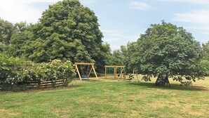 Zona enjardinada a l'aire lliure, amb un tobogan i un petit edifici de fusta, tot envoltat d'arbres.