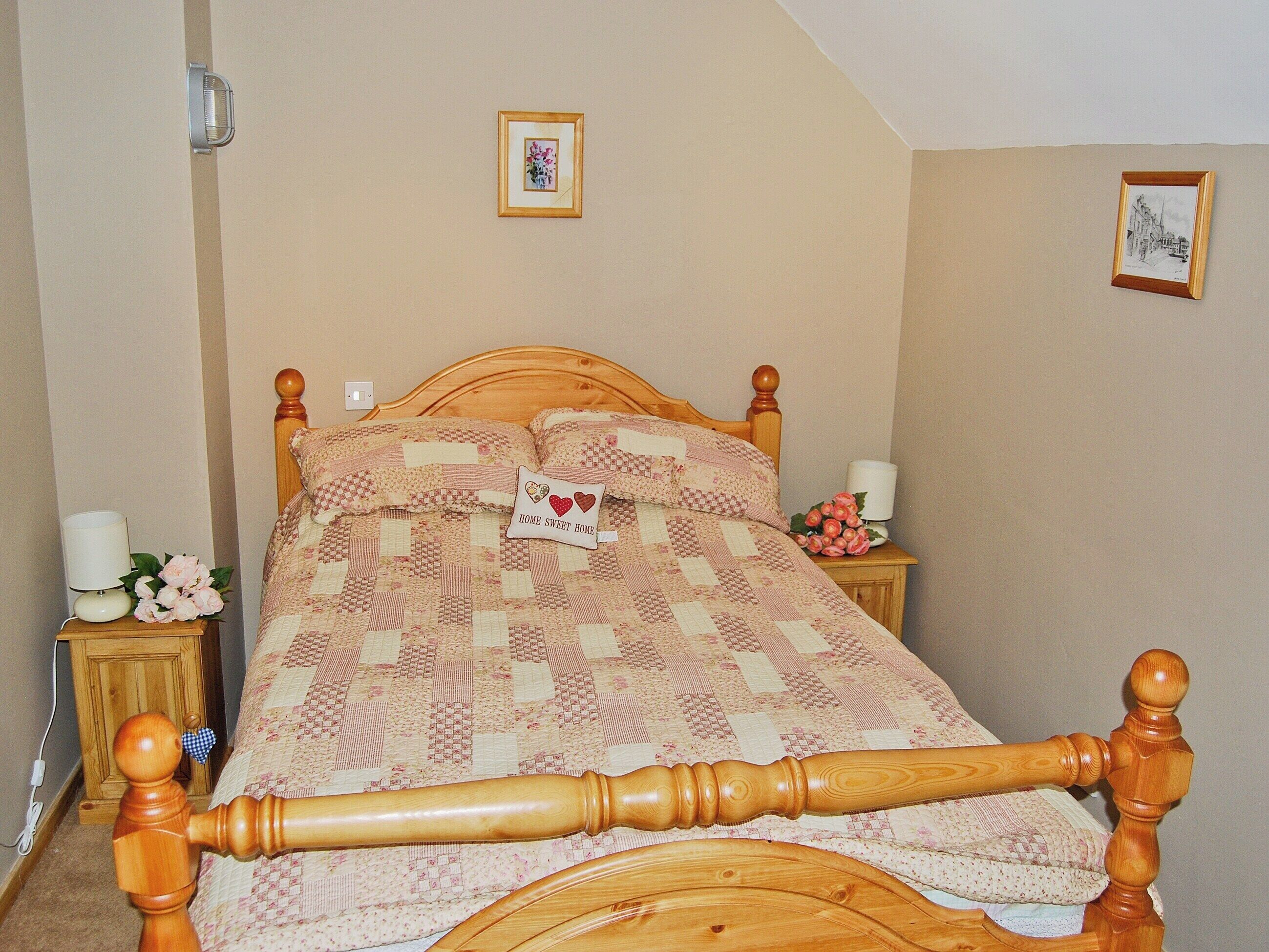 A bedroom with a wooden bed, a nightstand with a lamp, and a wall-mounted picture.