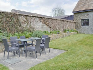 Un patio al aire libre con una mesa y sillas, un muro de piedra y un césped.