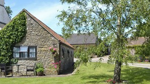 A stone building with a sloped roof, a small porch with chairs, and a tree in the foreground. - 1 bedroom accommodation in Priddy, near Wells (Priddy, near Wells)