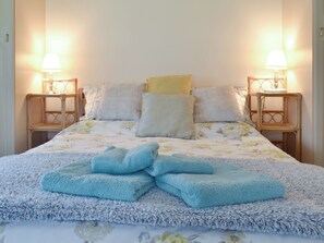 Ein ordentlich bezogenes Bett mit floralem Überwurf, mehreren Kissen und zwei Nachttischen aus Holz mit je einer Nachttischlampe.