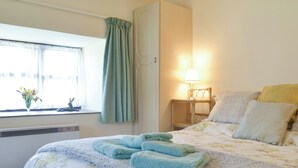 A hotel room with a bed, a window with curtains, a bedside lamp, and a vase with flowers on the windowsill. - 1 bedroom accommodation in Priddy, near Wells (Priddy, near Wells)