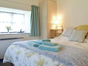 A hotel room with a bed, a window with curtains, a bedside lamp, and a vase with flowers on the windowsill.