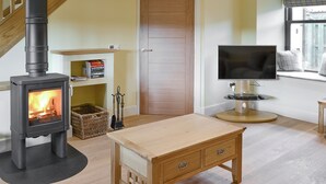 A living room with a wood-burning stove, a television, a wooden table, and a staircase. - 2 bedroom accommodation in Linlithgow, near Edinburgh (Linlithgow, near Edinburgh)