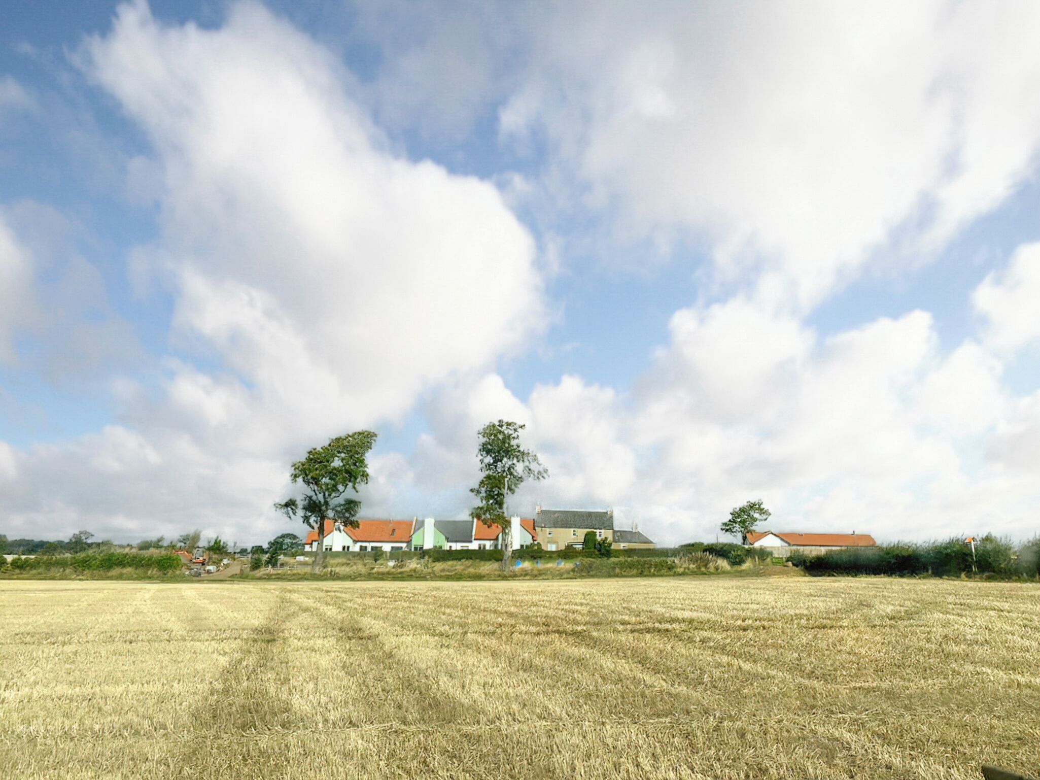 Un paisaje rural con un campo, algunas casas y un cielo despejado.