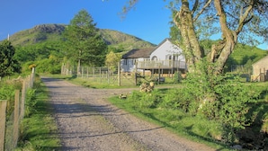 A rural road leading to a white house with a balcony, surrounded by greenery and a mountain in the background. - 4 bedroom accommodation in Taynuilt, near Oban (Taynuilt, near Oban)