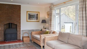 A cozy living room with a brick fireplace, wicker furniture, and a large window with curtains. - 4 bedroom accommodation in Taynuilt, near Oban (Taynuilt, near Oban)