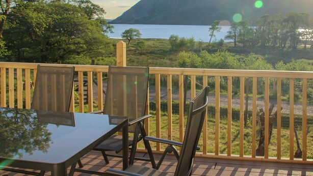 A deck with a table and chairs overlooking a lake and mountains. - 4 bedroom accommodation in Taynuilt, near Oban (Taynuilt, near Oban)