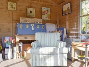 A cozy cabin interior with a striped armchair, wooden walls, a vintage suitcase, and various items on shelves. - 2 bedroom accommodation in Bonsall, near Matlock (Bonsall, near Matlock)