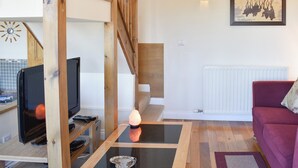 A living room with a wooden staircase, a television, a table with a lamp, a red sofa, and a painting on the wall. - 1 bedroom accommodation in Watermillock-on-Ullswater (Watermillock-on-Ullswater)