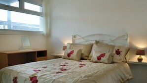 Ein ordentlich gemachtes Bett mit floralem Bettzeug, einer Nachttischlampe und einem Nachttisch mit Lampe.