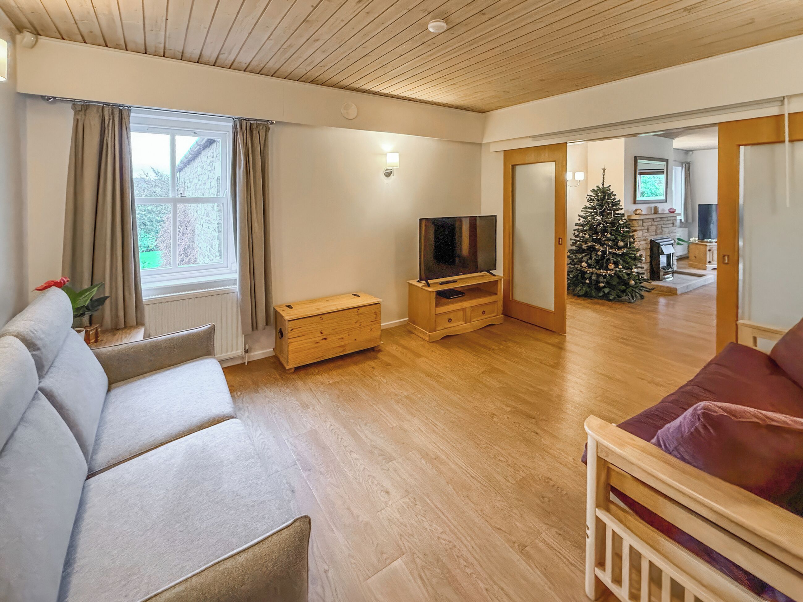 Una sala de estar con piso de madera, un sofá, un televisor sobre un mueble de madera, un árbol de Navidad y una chimenea.