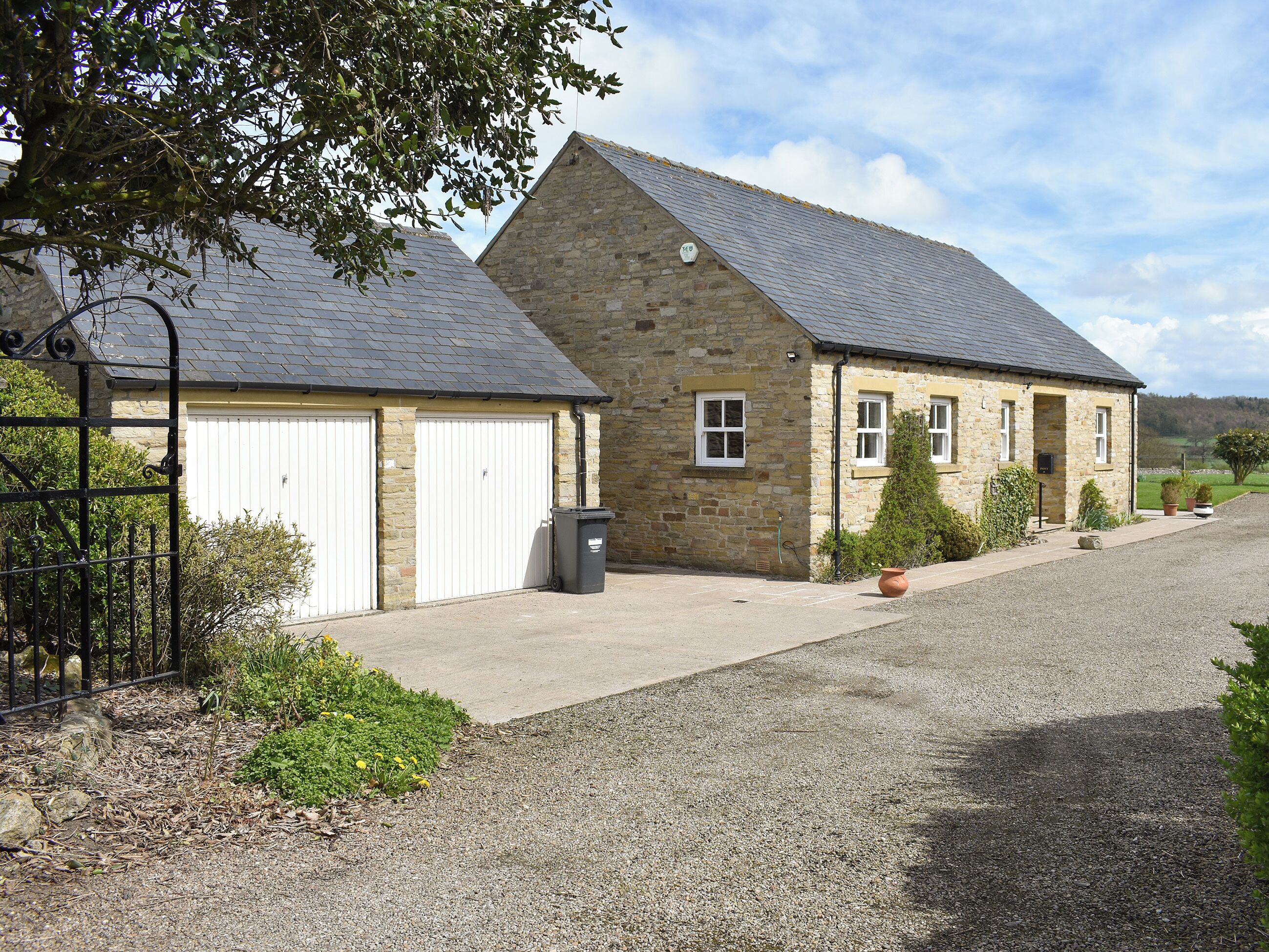A stone building with two garage doors, a gravel driveway, and potted plants.