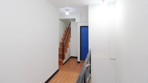 A narrow hallway with a staircase leading to a blue door. - Kamar Keluarga Bandara Mas Syariah (Tangerang)