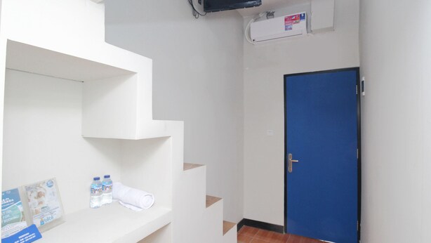 A hotel room with a blue door, white walls, a staircase, and a mounted TV. - Kamar Keluarga Bandara Mas Syariah (Tangerang)