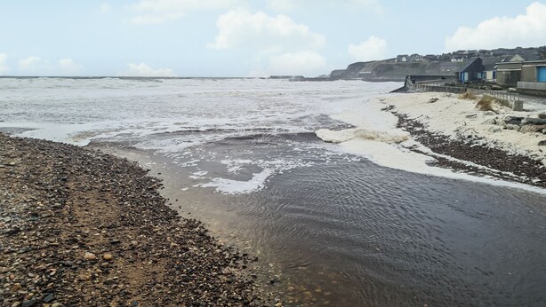 Eine Küstenansicht mit einem felsigen Strand, Wellen und einer in der Ferne liegenden Stadt mit Gebäuden.