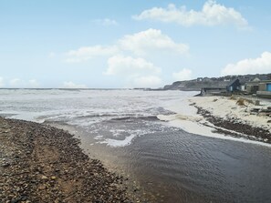 Een kustgezicht met een rotsachtig strand, golven en een in de verte gelegen stad met gebouwen.