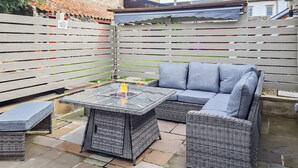 Ein Patio mit einem Tisch mit Glasplatte, einem grauen Sofa und Korbmöbeln.
