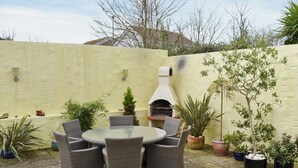 Un patio con mobiliario de mimbre, una mesa redonda, plantas en macetas y suelo de piedra.