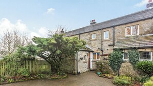 A stone house with a paved driveway, a wooden fence, and a tree in the yard.