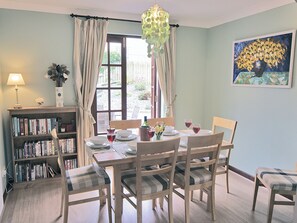 A dining room with a table set for four, a bookshelf, a painting, and a window with curtains.