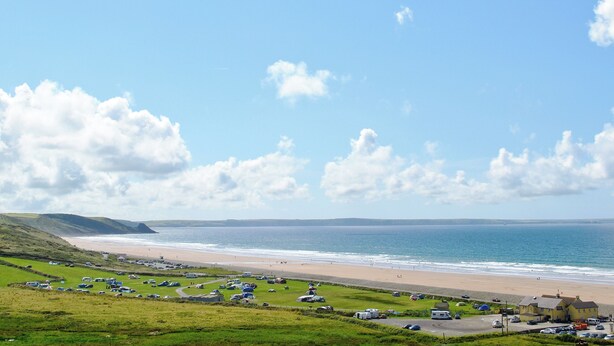 A coastal area with a beach, grassy fields, and parked vehicles. - Pebble Cottage - HW7447 (Broad Haven)