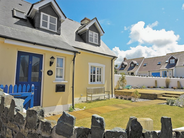 A two-story house with a blue door, a small porch, and a stone fence. - Pebble Cottage - HW7447 (Broad Haven)