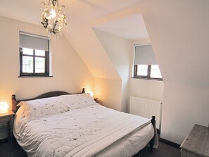 A bedroom with a bed, two bedside lamps, a chandelier, a window, and a radiator.
