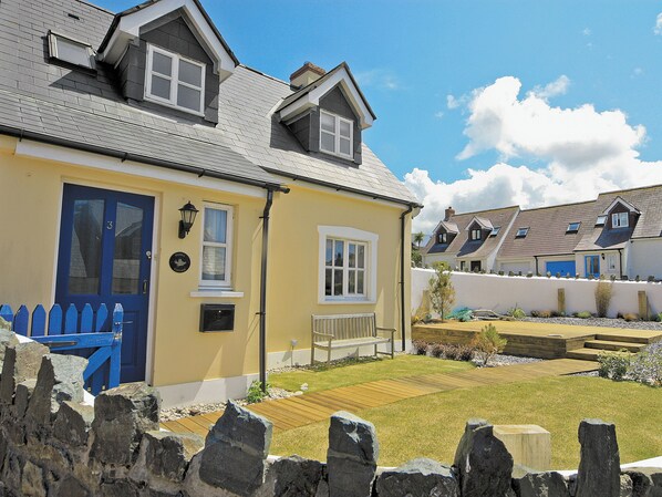 A two-story house with a blue door, a small porch, and a stone fence.