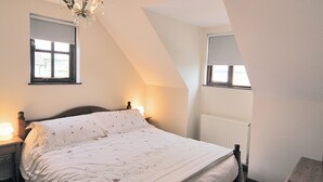A bedroom with a bed, two bedside lamps, a chandelier, a window, and a radiator. - Pebble Cottage - HW7447 (Broad Haven)