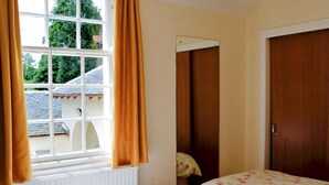 Ein Schlafzimmer mit zwei Betten, einem Fenster mit Vorhängen, einem Heizkörper und einer Tür.