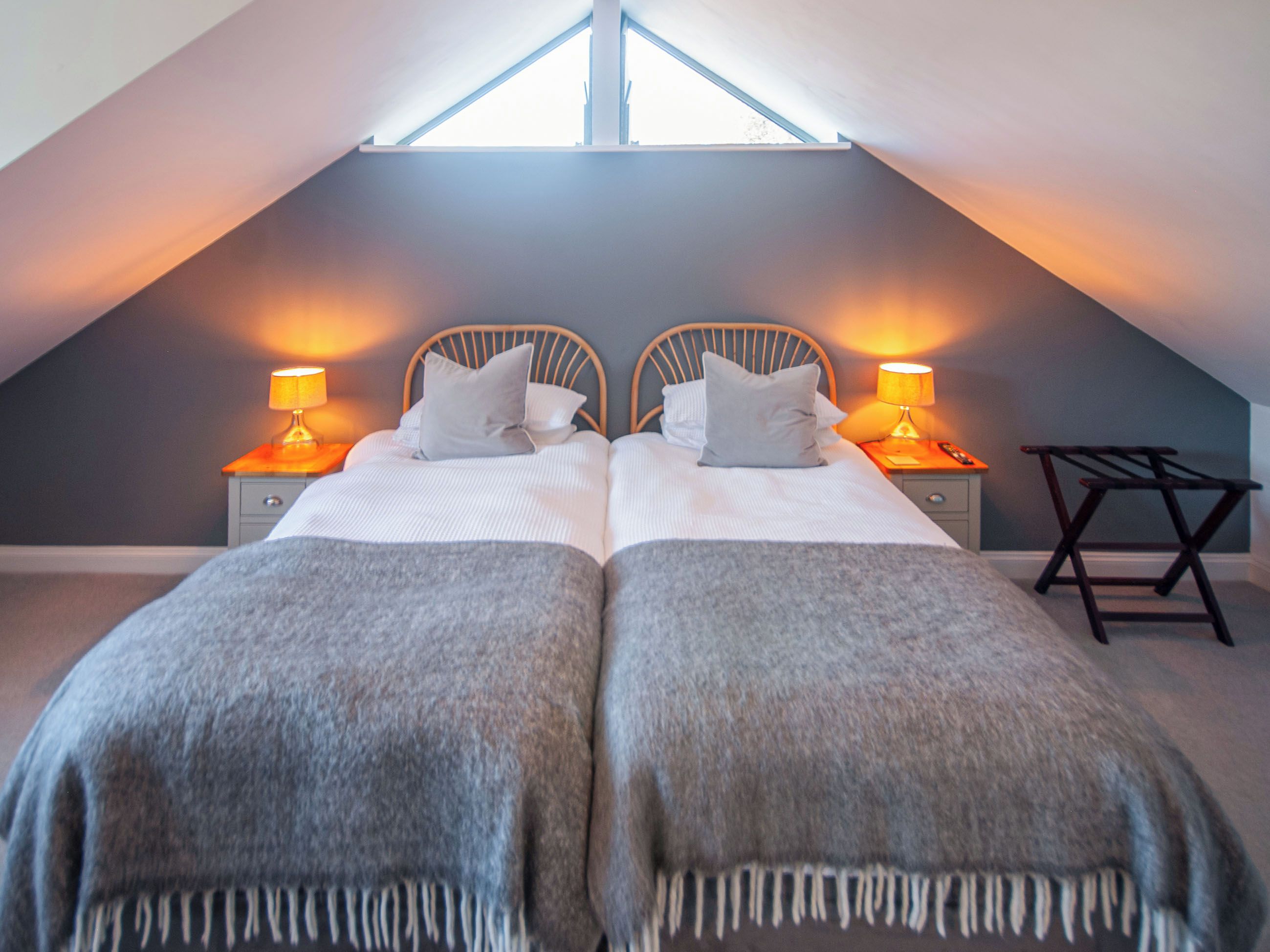 A bedroom with two beds, each with a nightstand and lamp, in a sloped ceiling room.