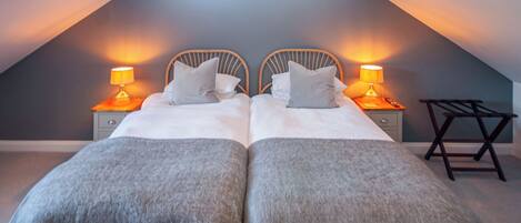 A bedroom with two beds, each with a nightstand and lamp, in a sloped ceiling room.