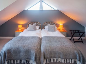 A bedroom with two beds, each with a nightstand and lamp, in a sloped ceiling room. - Red Squirrel Cottage (Whitwell, near Ventnor)
