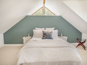 A bedroom with a sloped ceiling, a bed with white bedding, two bedside tables, and a window. - Red Squirrel Cottage (Whitwell, near Ventnor)